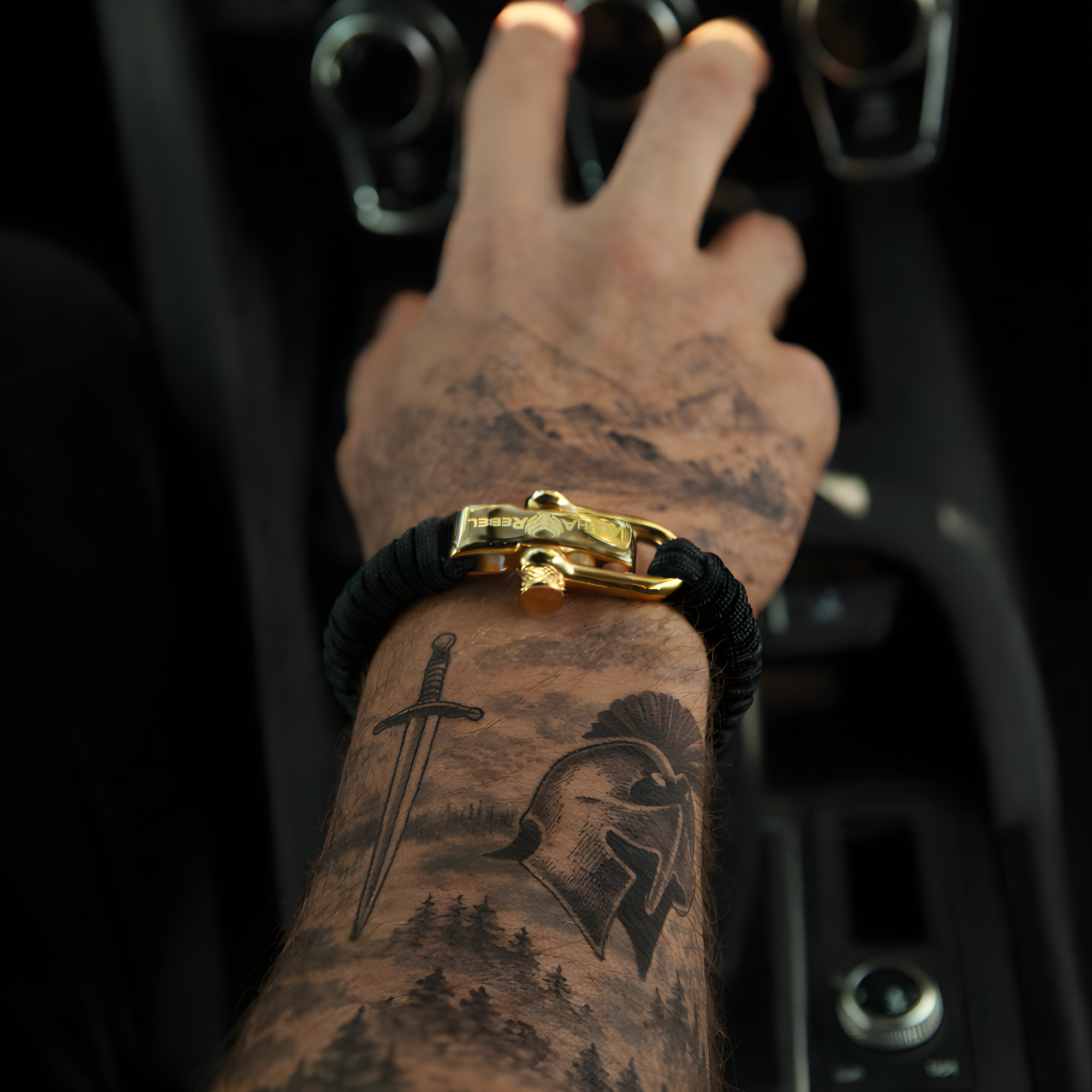 Hand with tattoos wearing a masculine luxury paracord bracelet with gold shackle inside a vehicle.