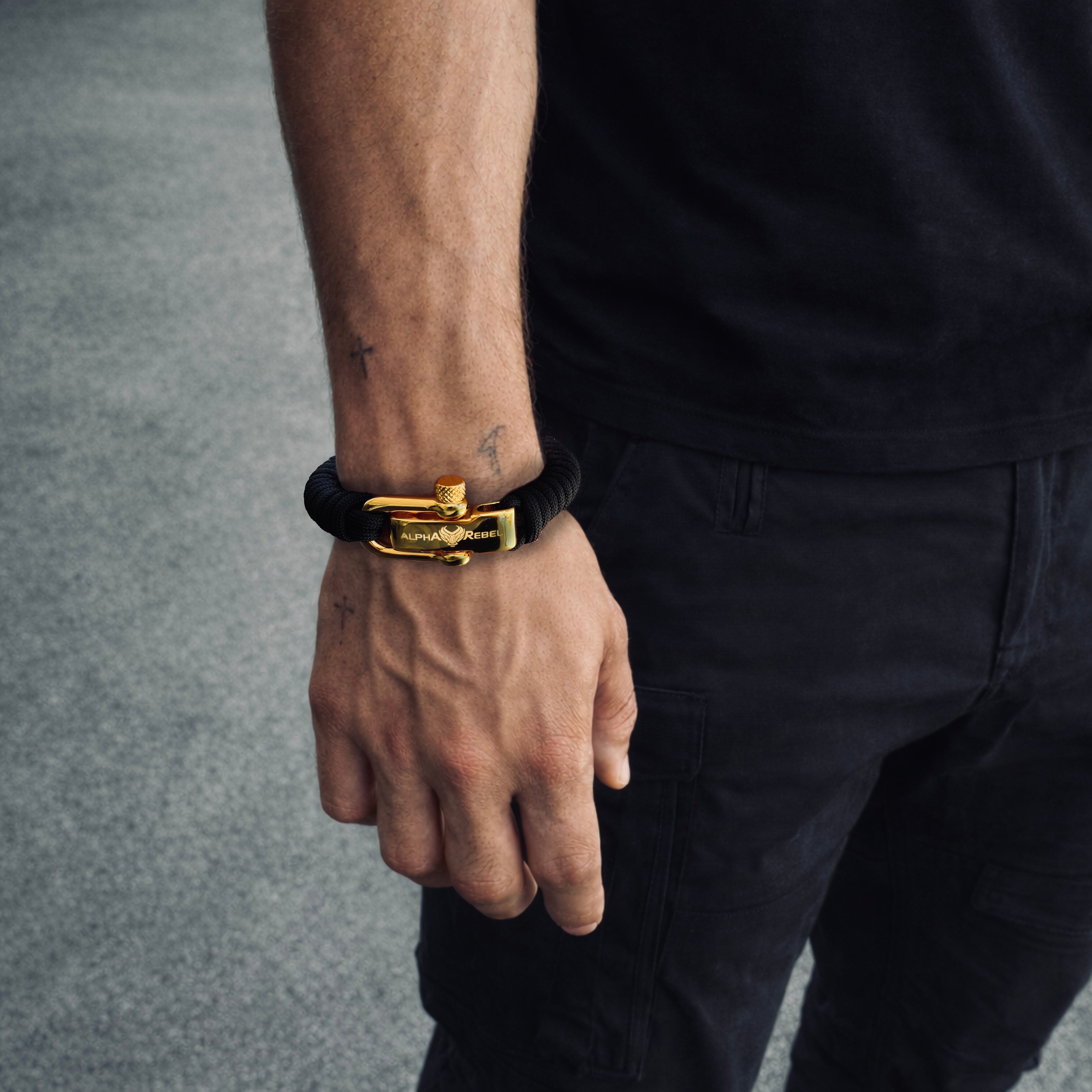 Person wearing a masculine luxury black paracord bracelet with a gold shackle on a gray background